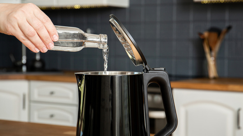 A hand pouring a bottle of vinegar into a black water kettle.