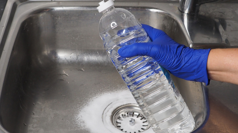 Gloved hand holding a bottle of vinegar ready to pour it into the sink with baking soda