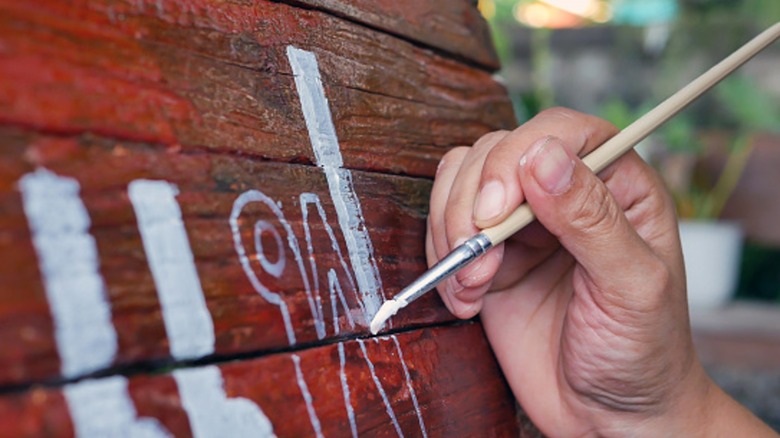 Person painting an outdoor sign with an artist's brush