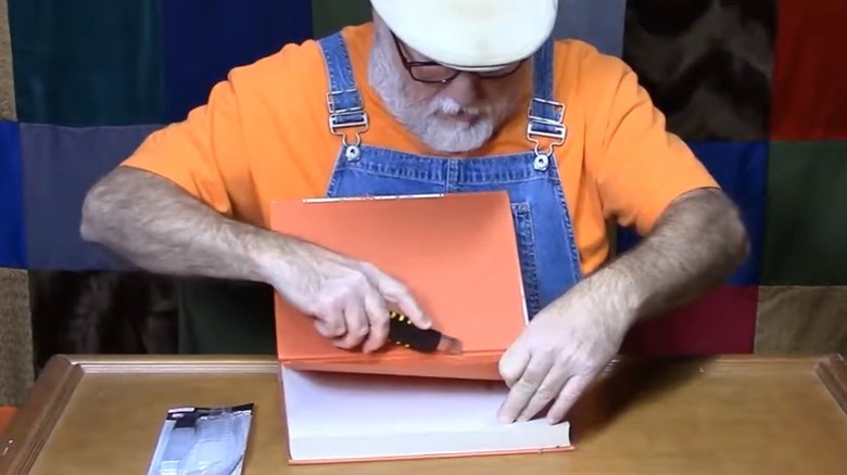 Man cutting through book cover with utility knife