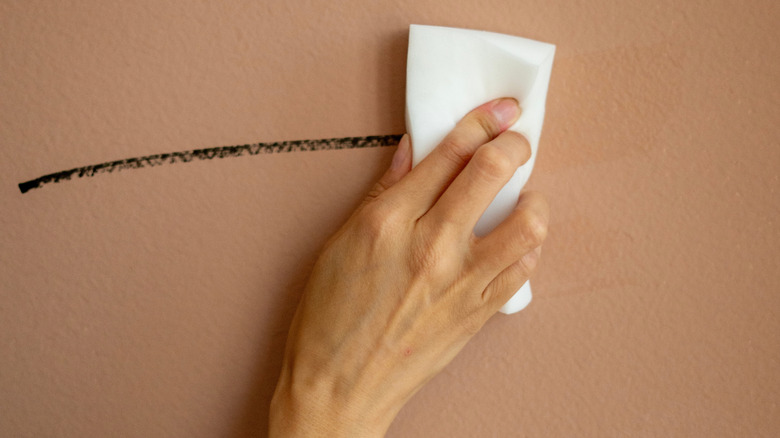 Hand holding melamine sponge, cleaning wall