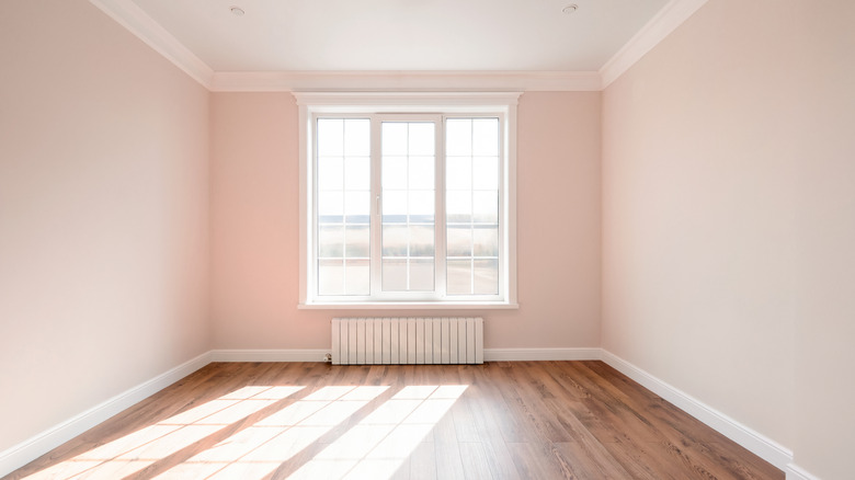An empty room with a sunny window and light pink walls with white trim