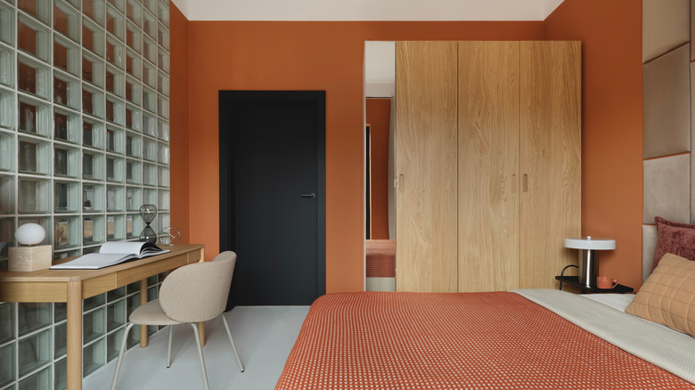 Bedroom with orange-clay walls, black door, desk, and bed