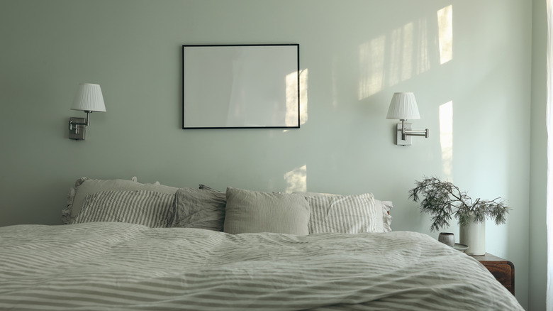 A soft green bedroom wall with sconces, bedside plants, and striped bedding