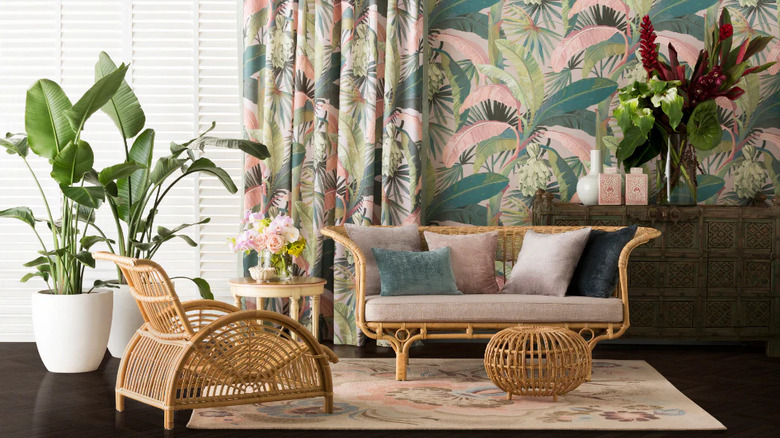 A bold pink and green palm wallpaper hangs in a living room full of rattan furniture