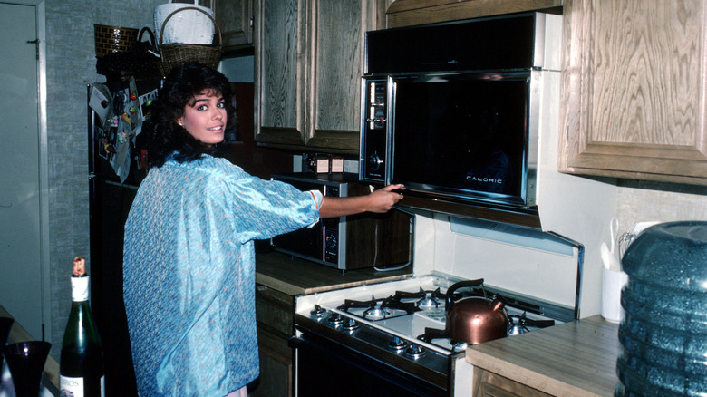 A person standing in a 1980s kitchen with woodgrain microwave