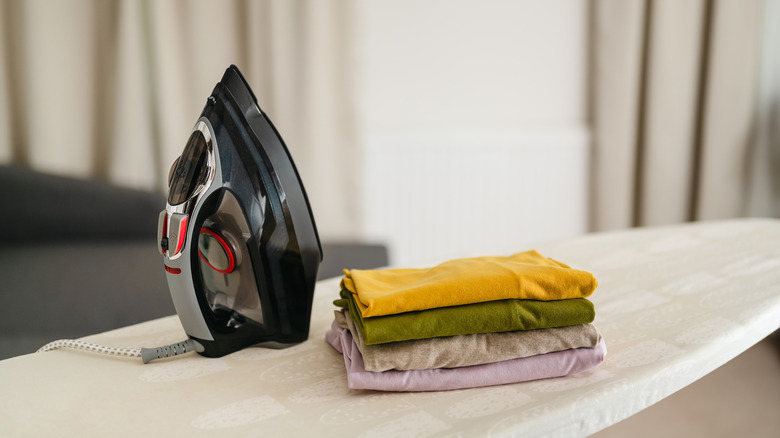Iron on ironing board next to folded clothes