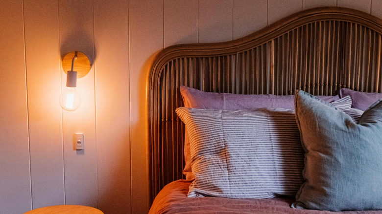 bed with soft pink bedding and unique wood headboard with a paneled wall behind