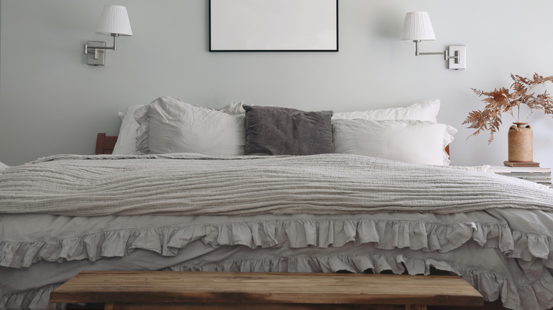 a bedroom with ruffled bedding and pillow cases in tones of gray and wood accents