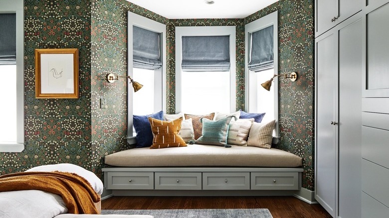 green wallpapered bedroom with bay window bench seating with pillows