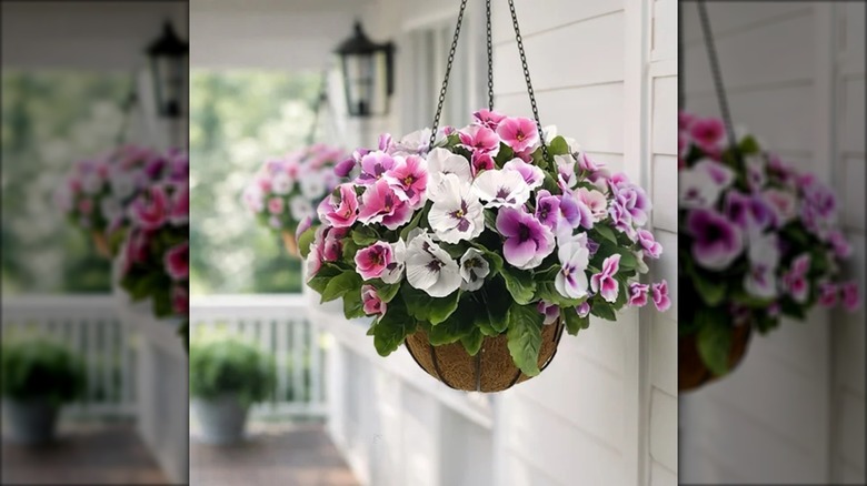A hanging basket with faux pansies hangs on a white painted porch