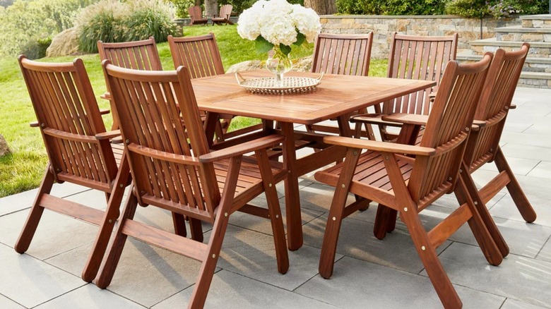 A large wooden outdoor dining set with eight seats and a floral centerpiece