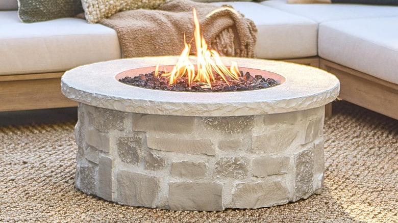 A fire pit in front of an outdoor couch with pillows and throw blankets