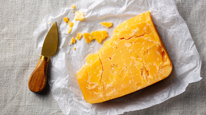 A piece of cheddar cheese and serving tool on parchment paper