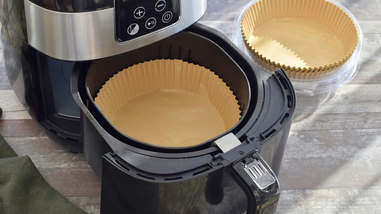 An open air fryer basket with a parchment paper liner inside