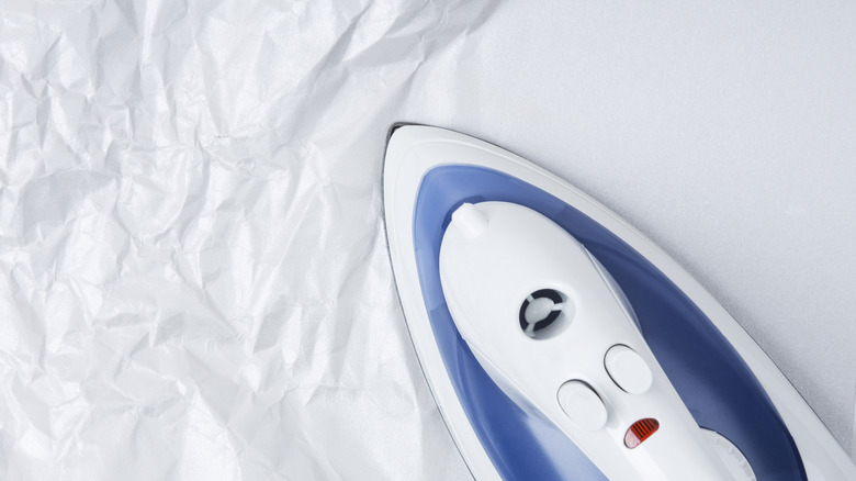 A clothing iron moving across wrinkled parchment paper