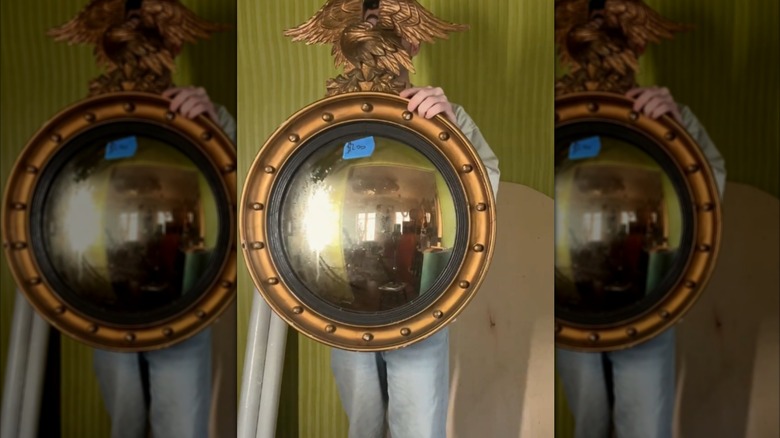 A young man holding up a round Federal mirror with an eagle on top