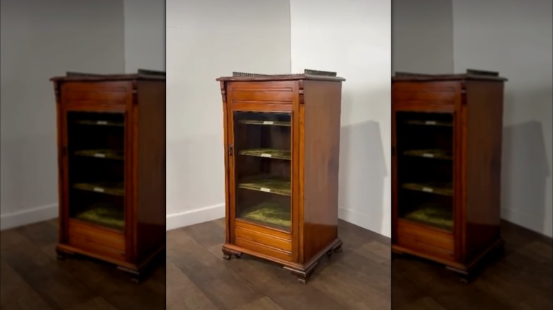 A wooden sheet music cabinet with green shelves and a glass door