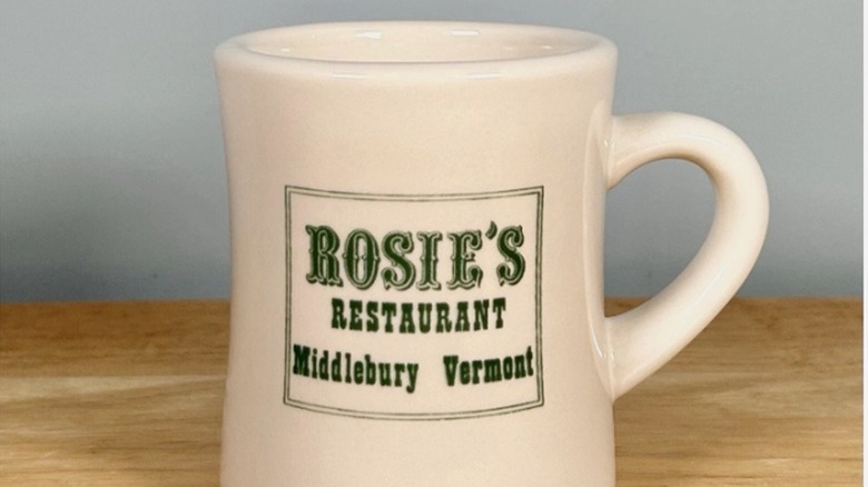 A white coffee mug displays the sign for Rosie's Diner in Middlebury, Vermont.
