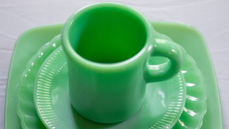 A green jadeite mug sits on a stack of green saucers.