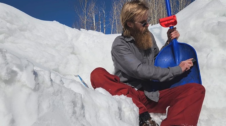 person applying Shovelwax to shovel while sitting in snow
