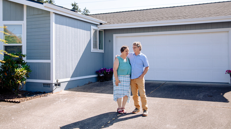 A couple stands outside a suburban home with asphalt driveway.