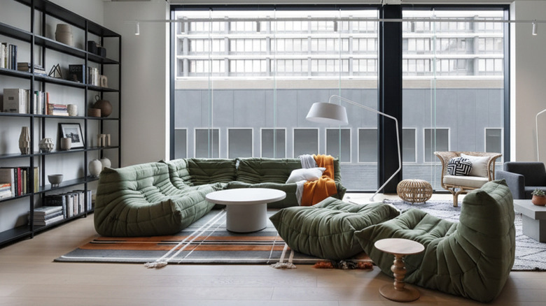 living room with a replica of the black leather and wood Eames lounge and ottoman in front of an exposed brick wall and floor-to-ceiling window with white drapery