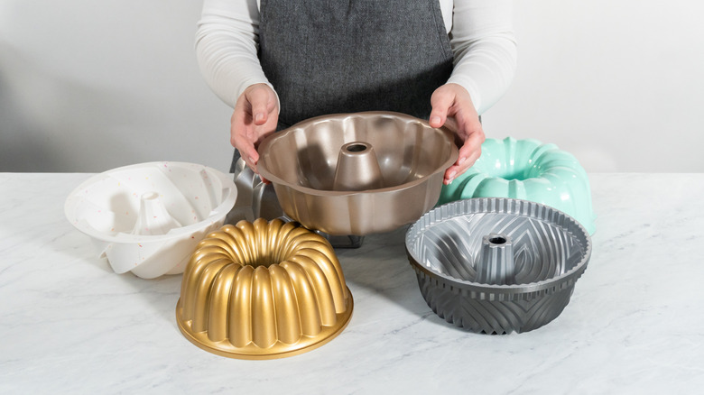 Person holding several bundt pans in different colors and sizes