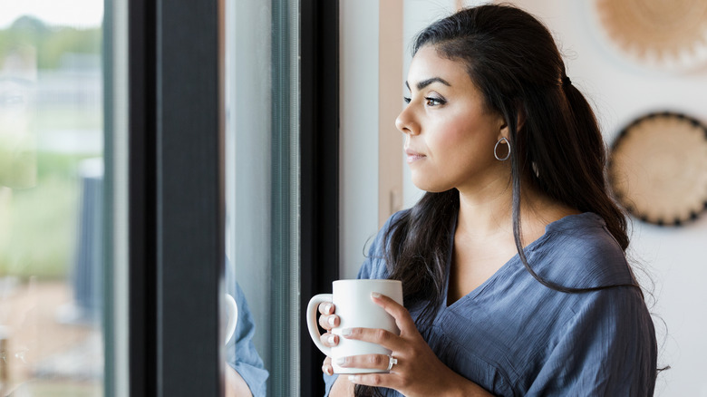 A woman looks out of a glass door while holding a mug