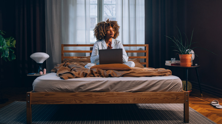 A woman sitting on the bed with a laptop in a large bedroom