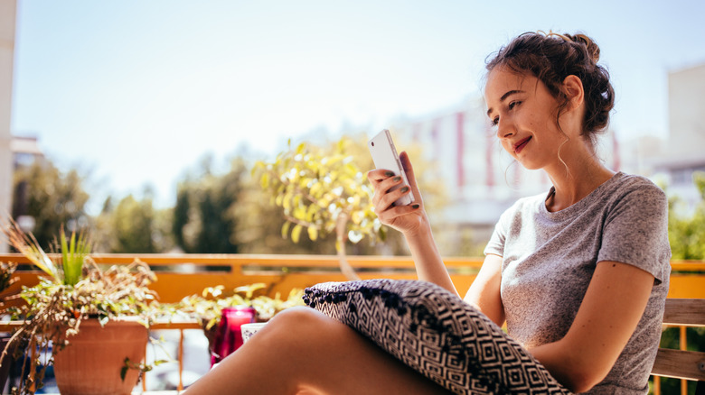 A woman looks at her phone while relaxing on a balcony patio
