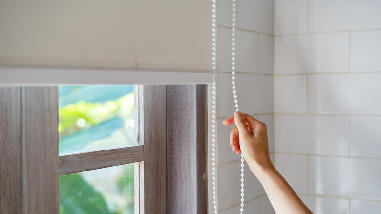 person pulling cord for roller shades in home