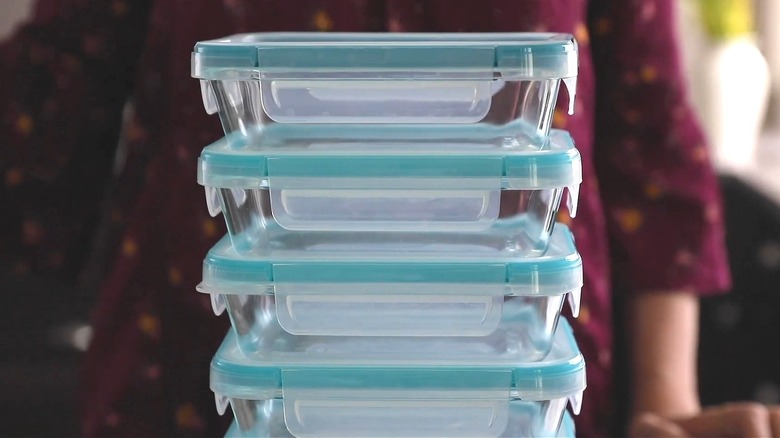 Person standing behind a stack of Pyrex glass containers on a table.