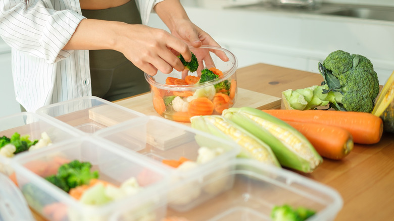 Woman adding vegetables to plastic food containers