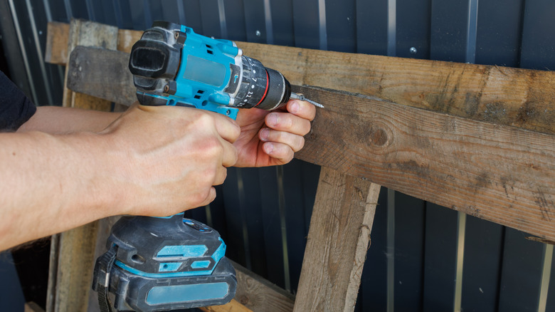 A person using a cordless drill on a wood pallet