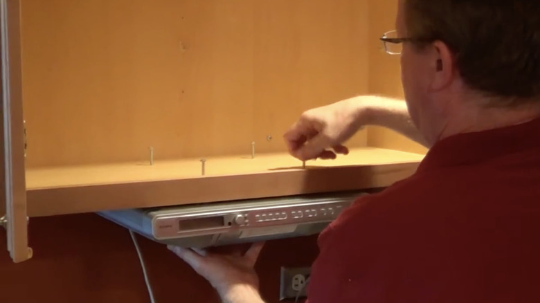 man installing the bolts on an under-cabinet kitchen music system