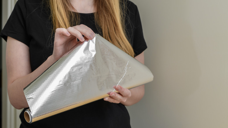 a woman opens a roll of aluminum foil