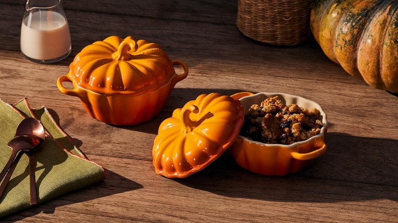 Two Le Creuset mini Pumpkin Petite Cocotte on a wooden table with fall accessories