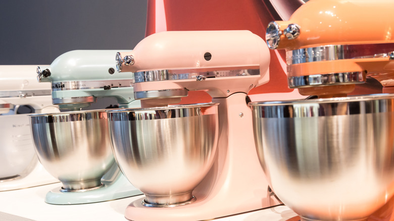 Three colorful KitchenAid mixers on a shelf