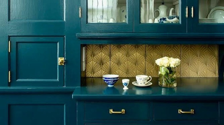 Gold art deco backsplash with leaf design alongside teal cabinets