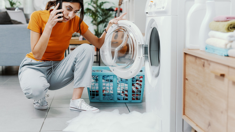 An alarmed woman on the phone looking at her overflowing washing machine