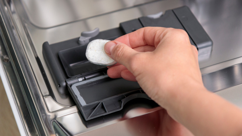 Hand putting a dishwasher tablet in the dispenser of a dishwasher