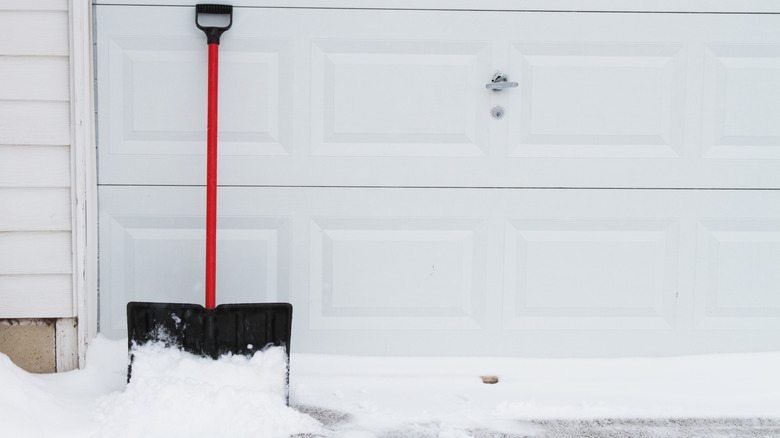 Snow shovel leaning against a garage door on a snowy driveway