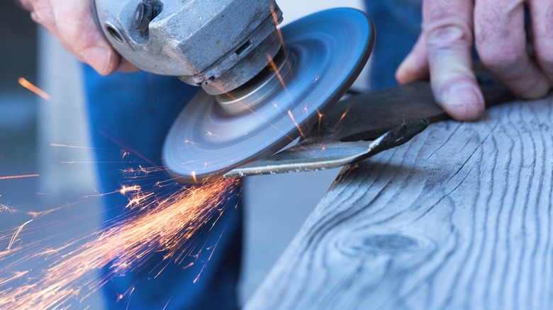 Person sharpening lawn mower blade with an angle grinder