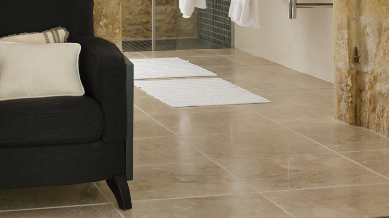 close up of bathroom with limestone floors, dual sinks, shower in the background, chair in the foreground, and rough stone walls