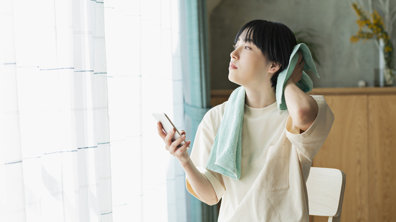 A person dries their hair and thinks in the bathroom while holding a phone
