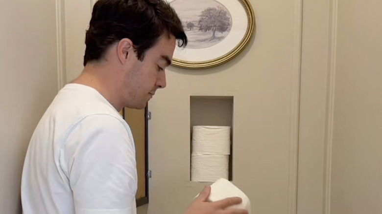 A man places toilet paper into a cavity in the wall