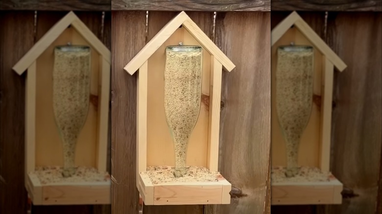 Gravity bird seed feeder made with an upside-down wine bottle mounted in a wood frame