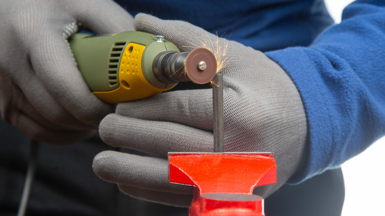 An individual using a Dremel tool to polish metal while wearing gloves