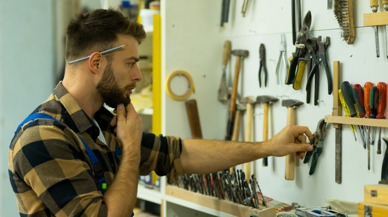 A man thinks while reaching for rusty tools in a garage